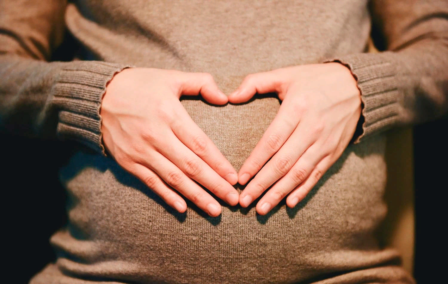 Беременная держит руки на животе в форме сердца