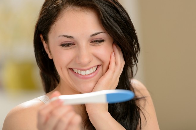 Девушка держит тест на беременность и улыбается